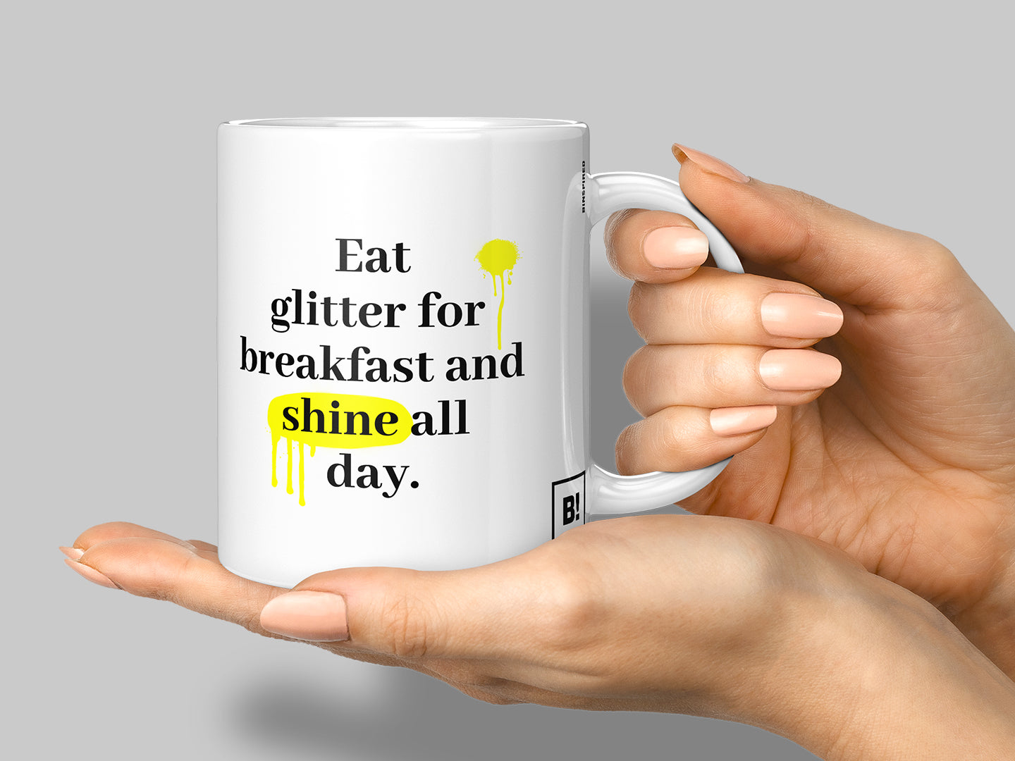 Hand holding a stylish mug from BINSPIRED's Everyday Quotes Mugs Collection, featuring an inspiring quote, set against a clean medium-light gray background for a modern and uplifting vibe.